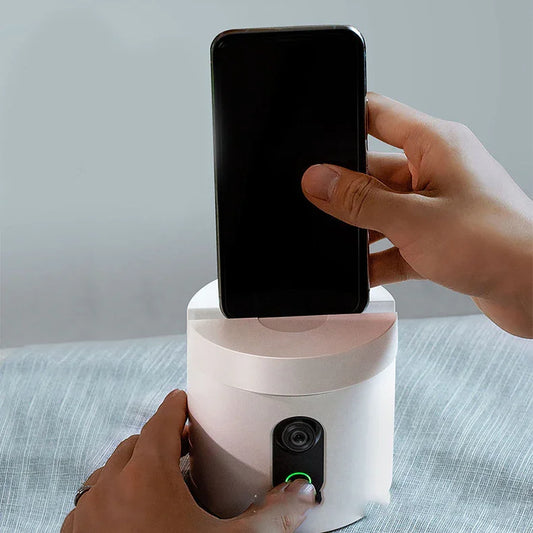 Hand placing smartphone on smart rotating camera device with button on desk