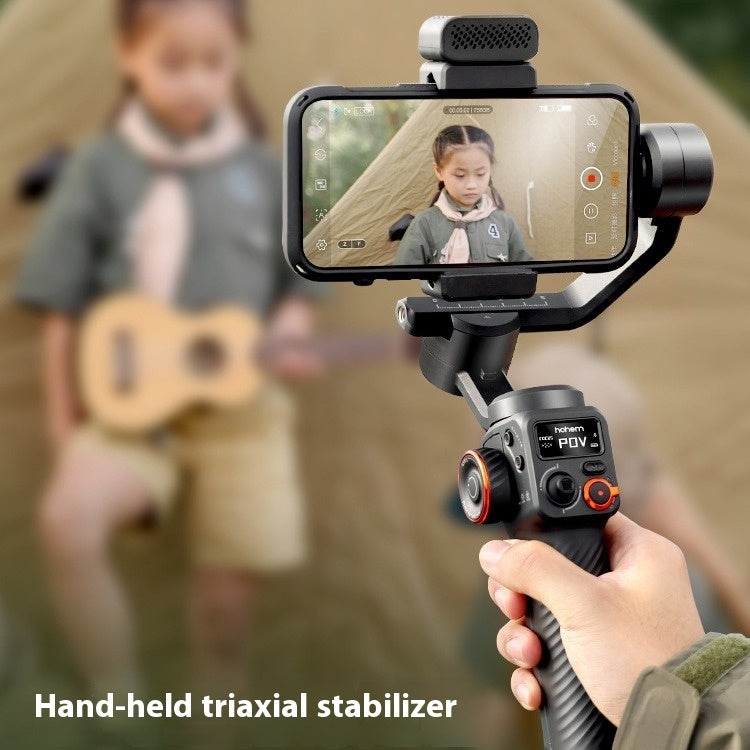 Hand-held triaxial stabilizer with smartphone filming a child playing ukulele near a tent outdoors
