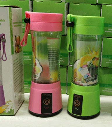Pink and green portable fruit blenders with clear containers and wrist straps, displayed on shelf with green boxes
